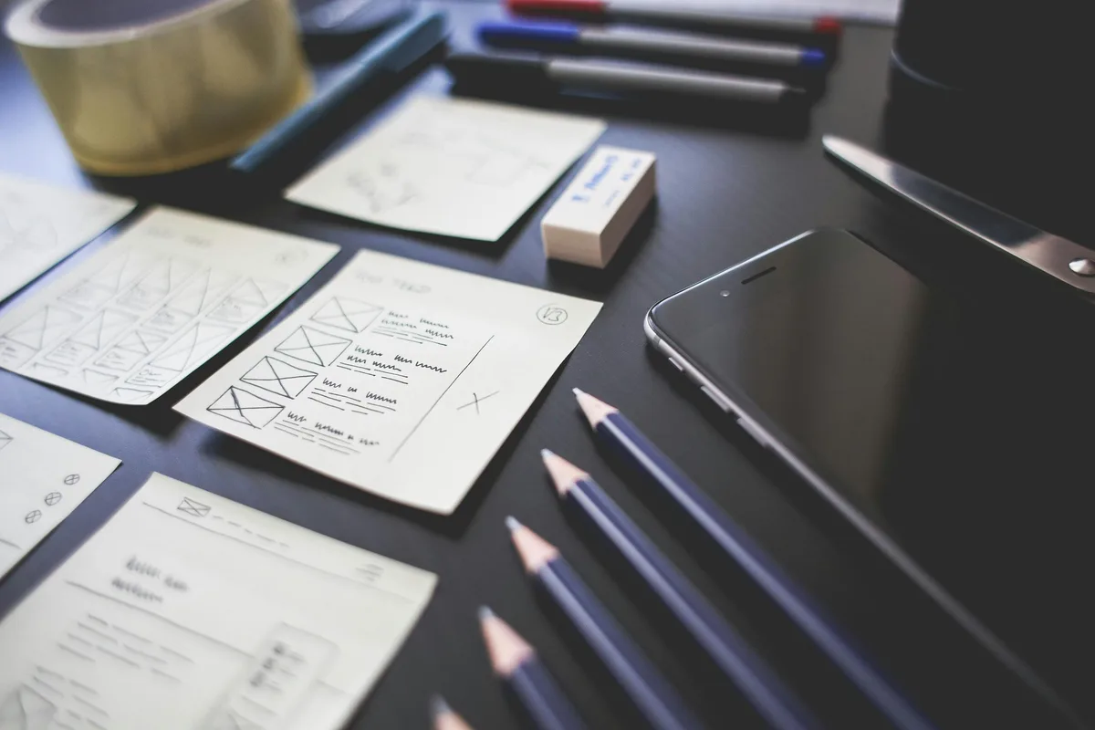 Handgezeichnete Wireframes für Seitenlayouts neben Stiften und Smartphone